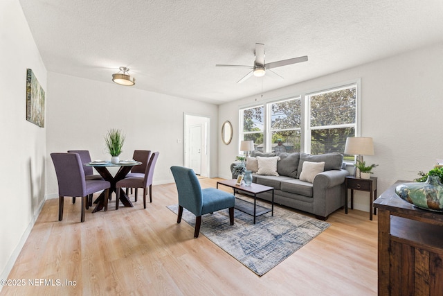 living area featuring light wood-style floors, ceiling fan, and a textured ceiling