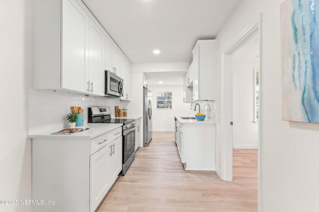 kitchen with stainless steel appliances, tasteful backsplash, light wood finished floors, light countertops, and a sink
