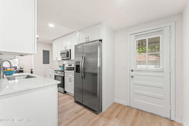 kitchen with stainless steel appliances, a sink, white cabinetry, light wood-type flooring, and light countertops