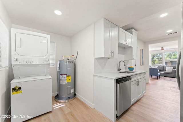 kitchen featuring estacked washer and dryer, electric water heater, stainless steel dishwasher, a sink, and light wood-style flooring