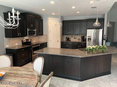 kitchen featuring stainless steel appliances, decorative backsplash, dark stone counters, an island with sink, and recessed lighting