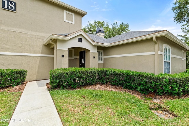 view of front of home featuring stucco siding, a front lawn, and a chimney