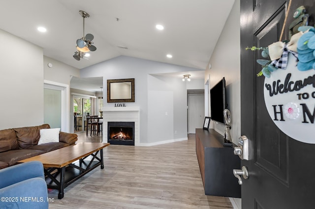 living room with vaulted ceiling, light wood-style floors, a tiled fireplace, recessed lighting, and baseboards