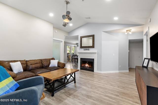 living room with vaulted ceiling, ceiling fan, a lit fireplace, and light wood-style flooring