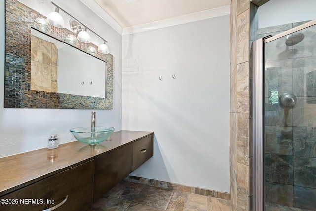 full bath featuring a stall shower, stone tile flooring, ornamental molding, vanity, and baseboards