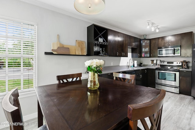 kitchen with stainless steel appliances, a sink, open shelves, dark brown cabinetry, and light wood-style flooring