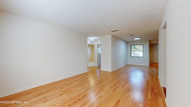unfurnished room with light wood finished floors, baseboards, and a textured ceiling