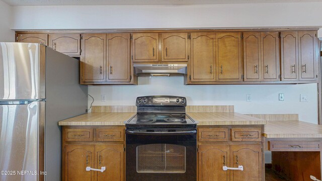 kitchen with under cabinet range hood, freestanding refrigerator, black / electric stove, and brown cabinetry
