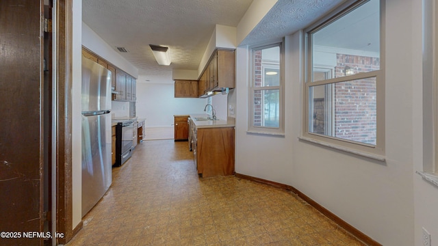 kitchen with brown cabinetry, range with electric cooktop, freestanding refrigerator, light countertops, and a sink