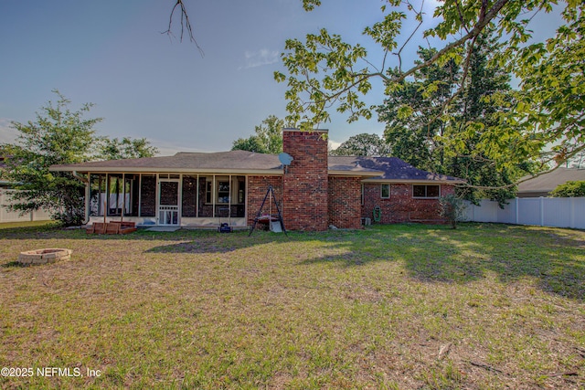 rear view of house with a sunroom, an outdoor fire pit, brick siding, and a chimney