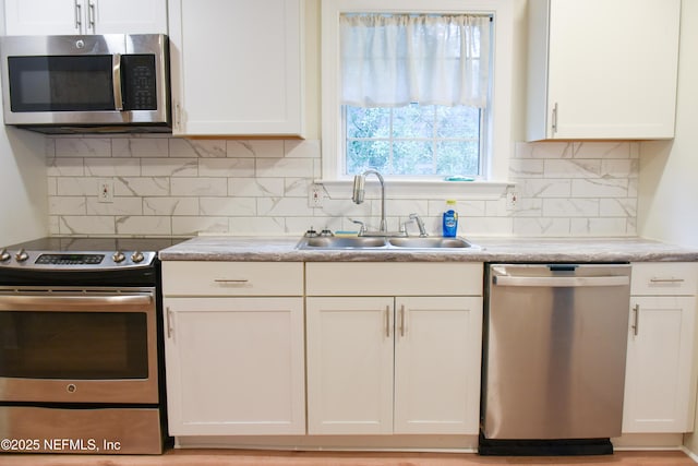 kitchen featuring stainless steel appliances, a sink, white cabinets, and backsplash