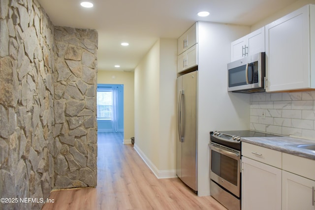 kitchen featuring stainless steel appliances, light wood-type flooring, white cabinets, decorative backsplash, and baseboards
