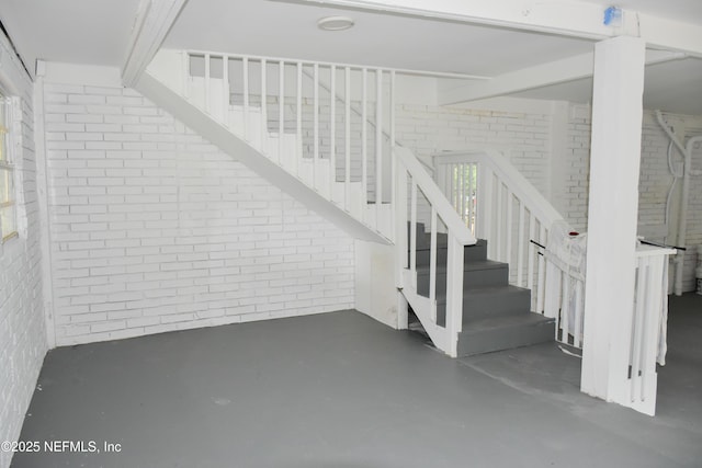 stairs featuring brick wall and concrete floors