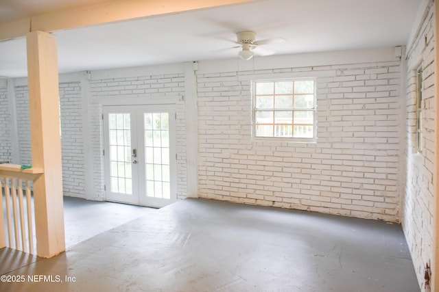 unfurnished room featuring brick wall, a ceiling fan, french doors, and unfinished concrete floors