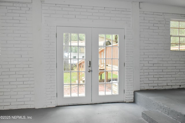 doorway to outside with french doors, unfinished concrete floors, and brick wall