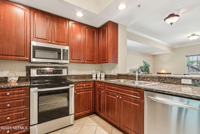 kitchen with appliances with stainless steel finishes, a sink, ornamental molding, light tile patterned floors, and dark stone countertops