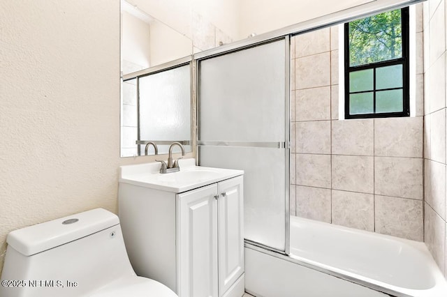 full bathroom featuring a textured wall, combined bath / shower with glass door, toilet, and vanity