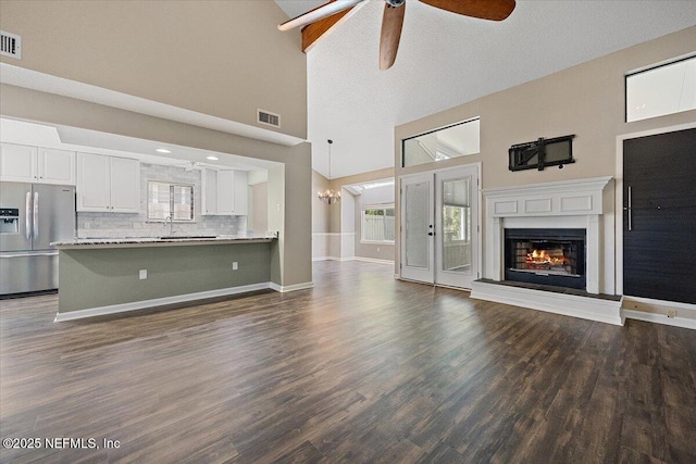 unfurnished living room with ceiling fan, a glass covered fireplace, dark wood-style flooring, a sink, and high vaulted ceiling