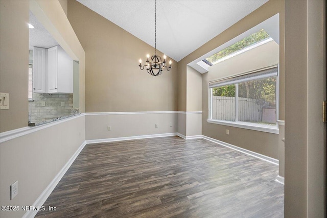 unfurnished dining area featuring a chandelier, dark wood-style flooring, baseboards, a skylight, and high vaulted ceiling