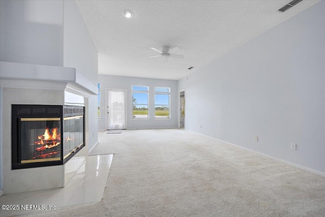 unfurnished living room featuring carpet, a textured ceiling, a multi sided fireplace, ceiling fan, and baseboards