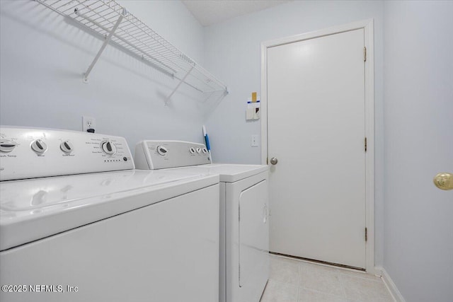 clothes washing area featuring washing machine and clothes dryer, light tile patterned flooring, and baseboards