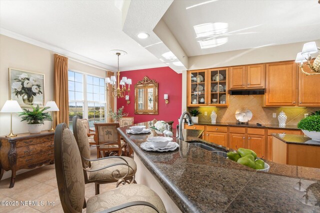 425 N Ocean Grande Dr Unit 205, Ponte Vedra Beach, FL 32082 - kitchen featuring brown cabinets, tasteful backsplash, glass insert cabinets, hanging light fixtures, and ornamental molding