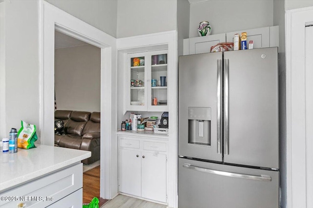 kitchen featuring stainless steel refrigerator with ice dispenser, light countertops, white cabinets, glass insert cabinets, and light wood finished floors