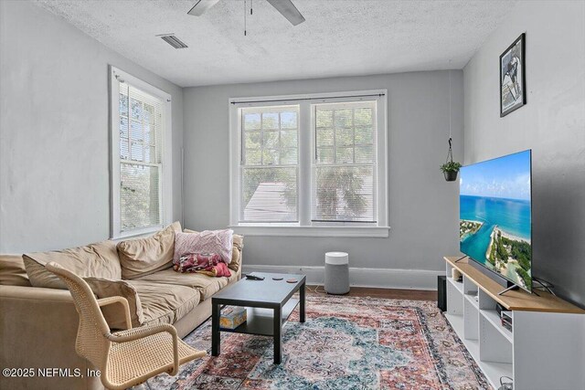 living area with a ceiling fan, a textured ceiling, wood finished floors, and baseboards