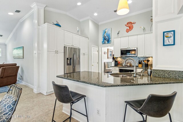 2738 Sea Grove Ln, Fernandina Beach, FL 32034 - kitchen featuring stainless steel appliances, a peninsula, tasteful backsplash, white cabinetry, and a breakfast bar area
