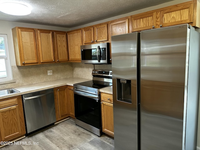 234 Canis St W, Orange Park, FL 32073 - kitchen featuring stainless steel appliances, light wood-style flooring, light countertops, brown cabinetry, and a textured ceiling