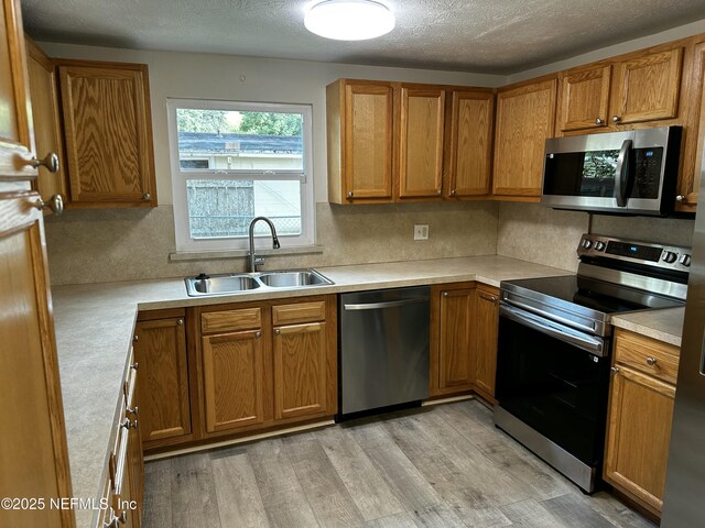 234 Canis St W, Orange Park, FL 32073 - kitchen featuring stainless steel appliances, a sink, brown cabinetry, light wood-style flooring, and a textured ceiling