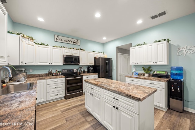 97054 Huntington Ct, Yulee, FL 32097 - kitchen with stainless steel appliances, a sink, white cabinets, light wood finished floors, and a center island
