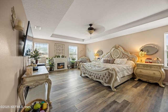 97054 Huntington Ct, Yulee, FL 32097 - bedroom with wood finished floors, a raised ceiling, a textured ceiling, a glass covered fireplace, and ceiling fan