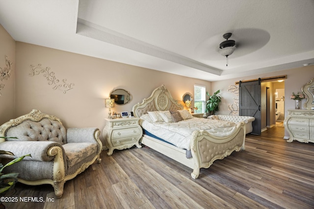 97054 Huntington Ct, Yulee, FL 32097 - bedroom with a barn door, a tray ceiling, wood finished floors, and a ceiling fan