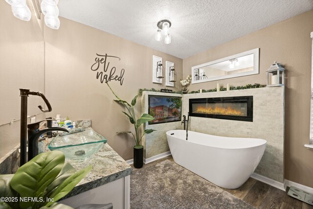 97054 Huntington Ct, Yulee, FL 32097 - full bath with a soaking tub, a glass covered fireplace, a textured ceiling, vanity, and baseboards