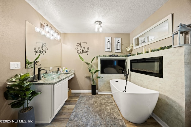 97054 Huntington Ct, Yulee, FL 32097 - bathroom with wood finished floors, a soaking tub, a textured ceiling, vanity, and baseboards