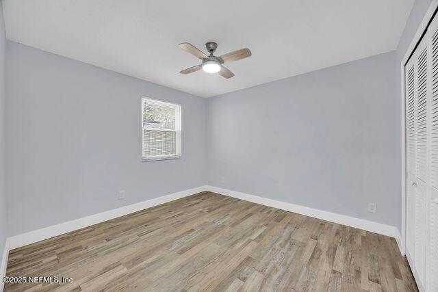 unfurnished bedroom featuring a closet, baseboards, wood finished floors, and ceiling fan