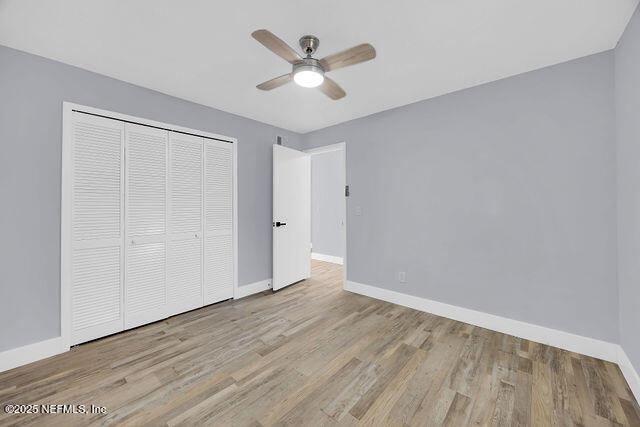 unfurnished bedroom featuring baseboards, wood finished floors, a closet, and a ceiling fan