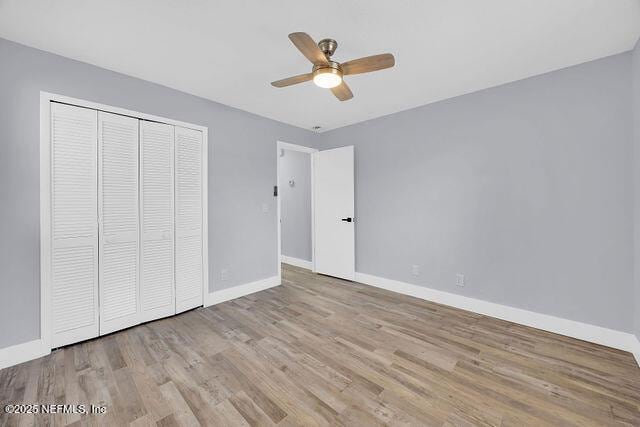 unfurnished bedroom with wood finished floors, baseboards, a closet, and a ceiling fan