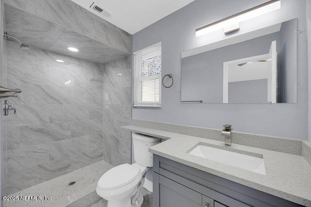bathroom featuring vanity, toilet, and a tile shower