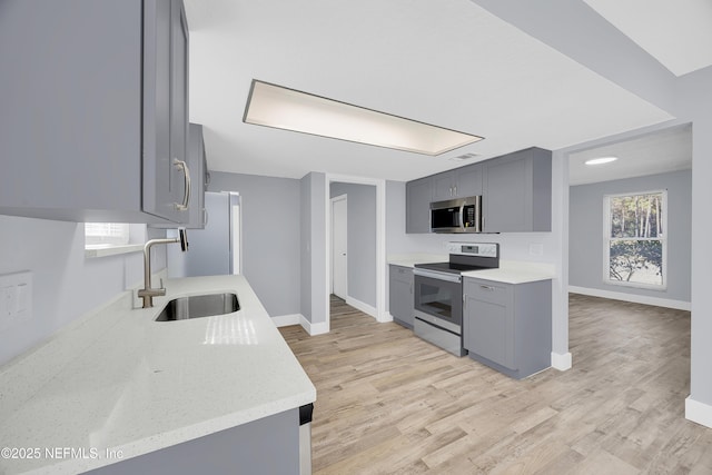 kitchen featuring stainless steel appliances, gray cabinetry, a sink, and light wood-style flooring