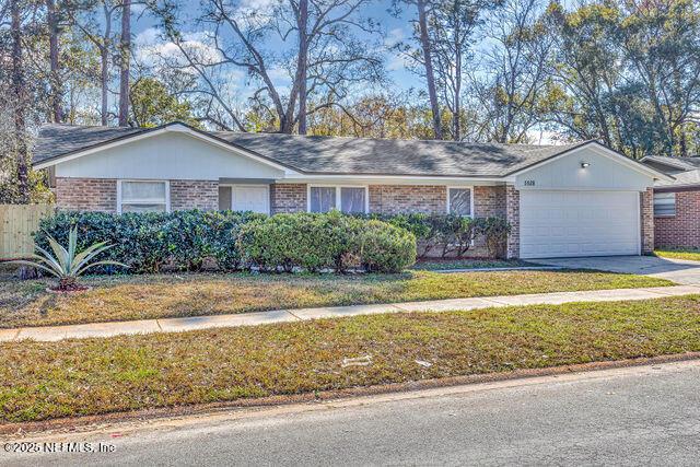 single story home with a garage, brick siding, driveway, and a front lawn