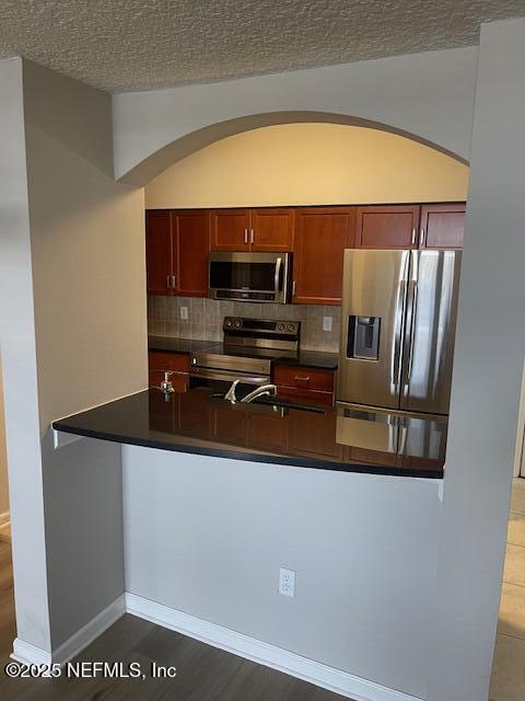 kitchen with stainless steel appliances, arched walkways, dark countertops, backsplash, and a textured ceiling