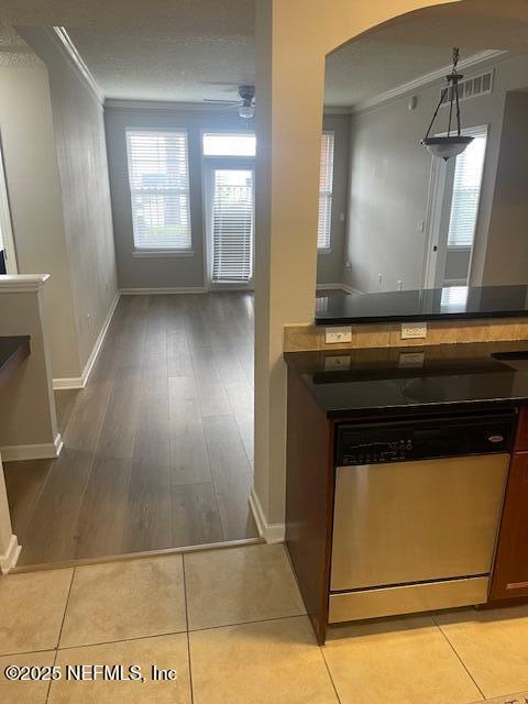 kitchen featuring stainless steel dishwasher, arched walkways, crown molding, healthy amount of natural light, and dark countertops