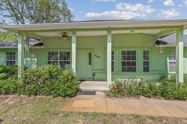 property entrance featuring stucco siding, ceiling fan, a shingled roof, and a porch