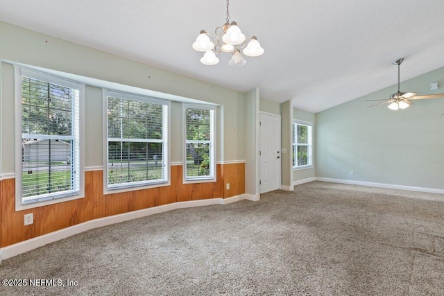 spare room with a chandelier, healthy amount of natural light, wooden walls, carpet, and vaulted ceiling