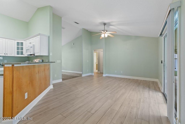 kitchen with white microwave, ceiling fan, lofted ceiling, light wood-type flooring, and white cabinets