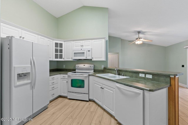 kitchen with white appliances, a sink, a peninsula, dark countertops, and lofted ceiling