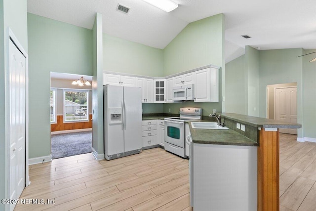 kitchen featuring white appliances, a sink, dark countertops, high vaulted ceiling, and a peninsula