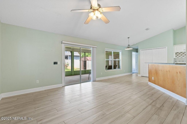 empty room featuring vaulted ceiling, light wood-style flooring, ceiling fan, and baseboards